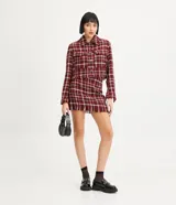 Campera corta de tweed a cuadros en tonos rojo, blanco y negro. Tiene cuello clásico, cierre frontal con botones, dos bolsillos en el pecho y flecos en el dobladillo.