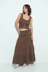 Falda larga maxi de algodón color marrón, con textura acanalada sutil. Presenta cintura elástica con cordón de ajuste y estructura en paños que añaden volumen y caída fluida.