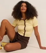 Blusa color amarillo claro confeccionada en tejido rib, con cuello polo marrón, manga corta y cierre frontal con botones marrones.