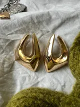 Par de aros dorados con forma geométrica irregular y diseño hueco.