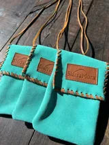 Funda para celular de gamuza azul marino con correa de cuero marrón y aplique de cuero marrón con logo de la marca.