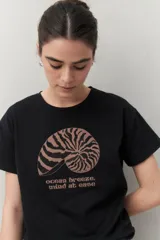 Remera blanca de manga corta con estampado de una concha marina y la frase "ocean breeze, mind at ease" en color marrón.