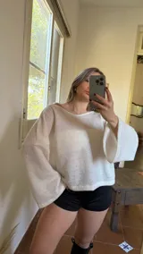 Blusa blanca de tejido suave, con escote en bote que puede usarse recto o caído en un hombro.