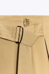 Pantalón color beige de tiro alto con cinturón ajustable con hebilla metálica. Presenta bolsillos laterales, de vivo en la pierna y de parche en la espalda.