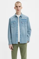 Camisa de denim celeste de corte recto, con mangas largas, cuello clásico, cierre con botones a presión, dos bolsillos con solapa abotonada en el pecho y canesú en la espalda.