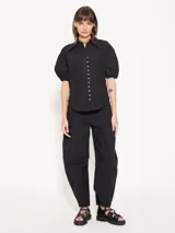 Pantalón negro de poplin 4way con lazo en la cintura, bolsillos ojales en delantero y espalda, pinza a la altura de la rodilla que le da una forma curvada, acceso mediante broche pantalonero, cierre y botón interno a tono de tela. Broches en el ruedo permiten ajustarlo.