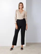 Enterito de fiesta con torso de lentejuelas color champagne, escote en V cruzado, mangas 3/4 con frunces en los hombros, cintura elastizada con lazo negro y pantalón negro de corte recto con bolsillos laterales.