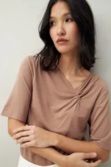 Remera de modal color marrón claro, de manga corta, con cuello asimétrico y detalle de nudo con frunces.