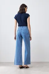 Pantalón de jean celeste de corte ancho, con cintura alta, pinzas y bolsillos laterales. Se ajusta a la cintura con un cinturón de cuero marrón.