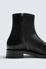 Bota de piel negra con punta fina, cierre de cremallera lateral y tacón bajo.