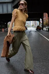 Pantalón de vestir color verde oliva, de tiro alto y pernera ancha, con pliegues delanteros, elástico en la espalda y cinturón marrón de cuero.