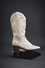 Botas cowboy de caña media color blanco hueso, con bordados decorativos en tonos beige y marrón claro en caña y puntera. Poseen punta afilada y tacón ancho de madera en tono marrón.