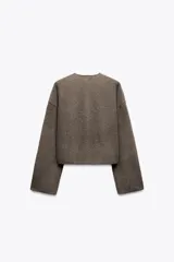 Chaqueta color crema de punto canalé con cuello redondo, manga larga y cierre frontal con botones marrones.