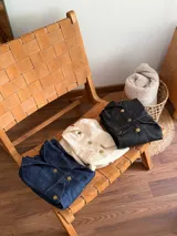 Vestido camisero corto de jean color crudo, con cuello camisero, cierre frontal con botones dorados, bolsillos con solapa en el pecho y mangas largas con puños abotonados.