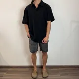 Chomba negra de corte oversize con cuello polo y tapeta de dos botones. Tejido de punto acanalado vertical.