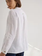 Camisa negra de lino con corte femenino, cuello clásico, cierre frontal con botones y mangas 3/4 con puños enrollados. Presenta detalles de frunces verticales en el frente y bolsillos de parche a la altura de la cadera.