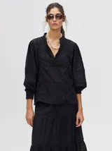 Camisa de broderie de algodón color negro, con cuello mao y cierre de cuatro botones. Presenta mangas abullonadas y galones con transparencias en la parte delantera y mangas.