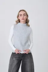 Chaleco de punto color crema, sin mangas, con cuello alto y textura acanalada vertical.