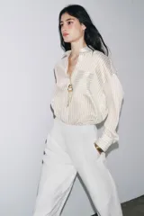 Camisa de manga larga con cuello solapa, a rayas verticales grises y blancas. Tiene un bolsillo de plastrón en el delantero y cierre frontal con botones.