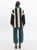 Buzo negro de fleece con cuello alto verde y cierre parcial con cremallera verde. Tiene puños con elástico azul y un bordado de un diamante blanco en el pecho.