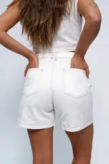 Short blanco de gabardina con pespuntes rojos, tiro medio/alto, tablones delanteros, bolsillos delanteros y traseros estilo jean. Presenta un logo bordado en rojo en la pierna derecha.