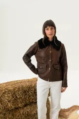 Chaqueta marrón de cuero con cuello de piel sintética negra, cierre con botones a presión, bolsillos con solapa y corte a la cintura.
