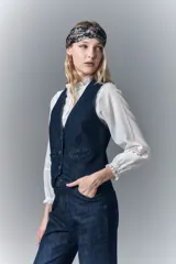 Chaleco sastrero de denim azul oscuro con elastano, acceso con botones con logo, falsos bolsillos ojal y tira de ajuste en la espalda con hebilla. Bordado de alas en la espalda.