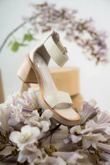 Sandalias de cuero color crudo, con tira ancha sobre los dedos, pulsera con hebilla al tobillo y taco cuadrado de madera.