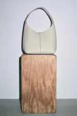 Bolso tipo saca de cuero color gris claro con textura granulada. Tiene asa de hombro y cierre con imán. Incluye cartera interior extraíble con bolsillo.