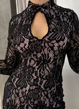 Vestido corto de encaje negro con forro color piel, cuello alto con abertura en el pecho y mangas largas acampanadas.