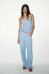 Pantalón denim celeste de tiro medio con cintura ajustable con cordones, bolsillos laterales y de plastrón en espalda. Cierre frontal con cremallera y gancho metálico.
