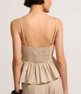 Blusa sin mangas color beige, con escote en V, breteles finos ajustables y peplum con volados en el bajo. Presenta lastex fruncido en la espalda.