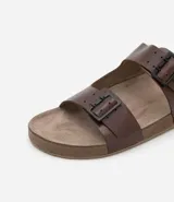 Sandalias tipo slide de cuero color marrón con dos tiras anchas ajustables con hebillas metálicas. Suela plana con textura. Marca Viko.