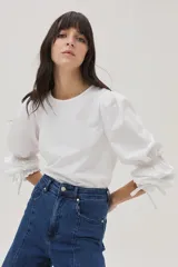 Blusa blanca de mangas largas abullonadas con puños elásticos y lazos.