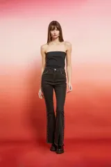 Pantalón de jean de tiro alto, color marrón oscuro con efecto lavado o desgastado, corte flare y tajo en el bajo. Presenta tachas doradas a lo largo de las costuras laterales.