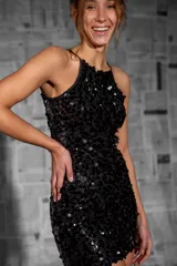 Vestido corto negro con lentejuelas grandes, escote halter y tirantes finos.