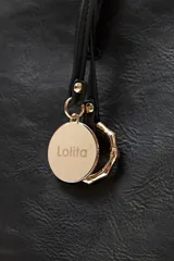 Cartera tote negra de cuero sintético con doble asa de hombro y dije metálico circular con el nombre de la marca.