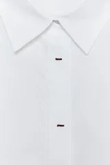 Camisa blanca oversize de popelina de algodón, con cuello solapa, manga larga con puños y cierre frontal con botones ocultos. Detalle de hilo de contraste en los botones.