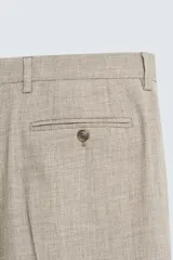 Pantalón de vestir para hombre, color beige claro con textura de tejido de lana. Presenta un corte regular fit, con pliegues marcados en el frente, bolsillos laterales y bolsillos traseros de doble vivo con botón.