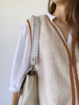 Bandolera color crudo con solapa de gamuza y cuerpo de cuero sintético texturizado. Tiene correa corta de cuero con tientos y forro de tela con bolsillo interno.