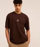 Remera marrón de corte relajado, cuello redondo y mangas cortas. Estampa frontal con un auto y la frase "Mindnight Legends Never Fade".