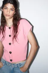 Top rosa de punto con cuello redondo y manga corta. Cierre frontal con botones en forma de corazón plateados.