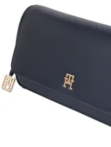 Cartera cruzada de mujer color azul marino, de material sintético liso, con solapa frontal y herrajes metálicos dorados. Presenta un monograma TH en el centro de la solapa y un charm colgante con el logo TH en el lateral.