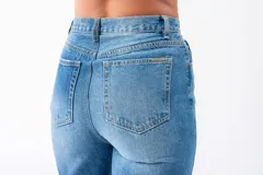Pantalón de jean azul de tiro alto con corte irregular en la cintura y cierre con doble botón.