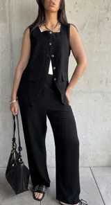 Conjunto negro de chaleco con botones y pantalón de vestir de corte recto. El chaleco tiene cuello cuadrado con ribete blanco y bolsillos delanteros. El pantalón es de tiro alto y pierna ancha.