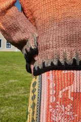 Sweater tejido a mano de lana merino con cuello redondo, mangas largas y calce holgado. Presenta un diseño degradado en tonos amarillo, naranja y marrón, con bordes en negro.