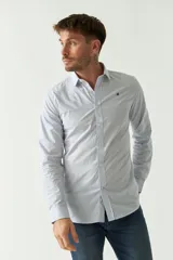 Camisa de hombre a rayas verticales celestes y blancas, corte slim fit, manga larga, logo bordado en el pecho y cartera con botones.