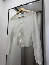 Saco tejido de crochet color blanco, de mangas largas y escote en V con lazos y borlas.
