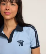 Blusa polo celeste de algodón con cuello y mangas cortas con ribete azul marino. Bordado "Seattle 78" en azul marino en el pecho.
