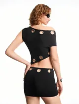 Conjunto negro de top de hombro oblicuo y minifalda, ambos con detalle de ojalillos metálicos.